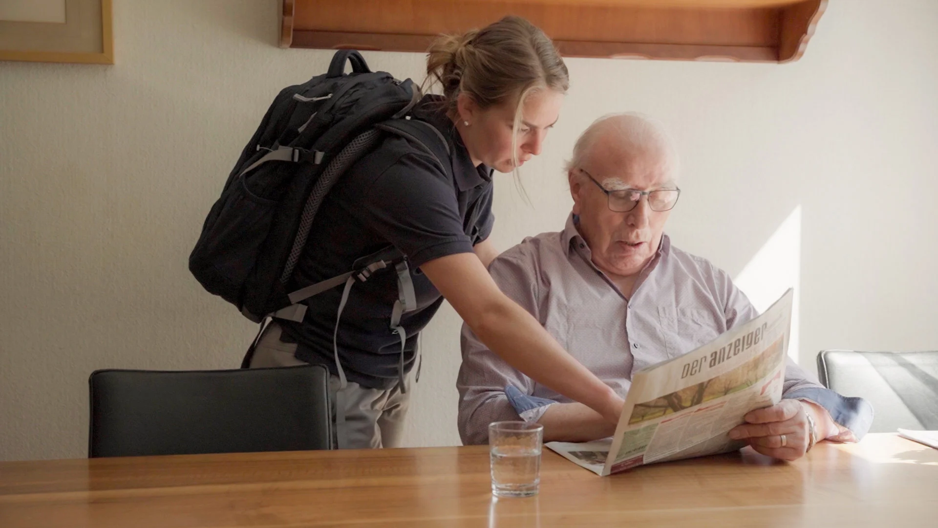 Spitex Aaregürbetal caregiver supporting an elderly man reading a newspaper at the dining table.