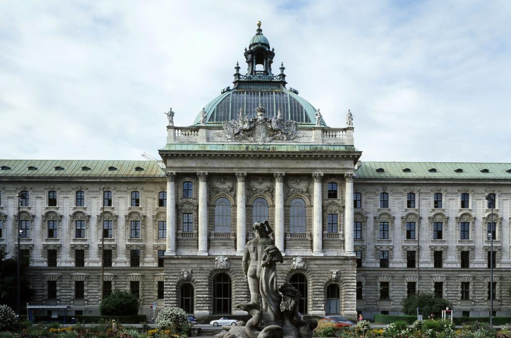 Neoclassical stone building facade with central dome, Corinthian columns and fountain statue in front under cloudy sky