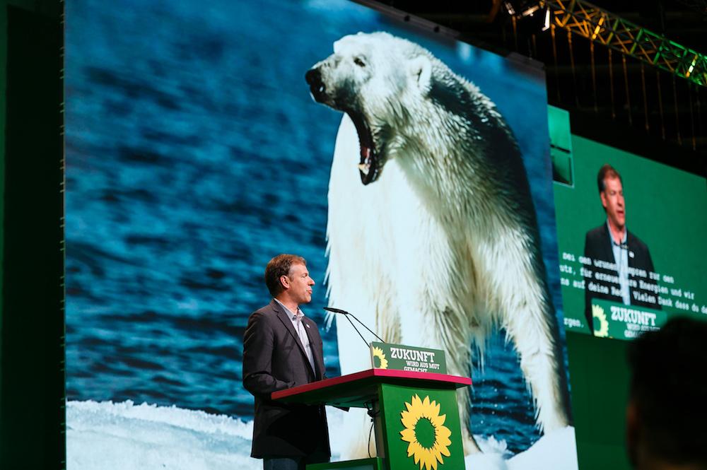 Man speaking at a podium with a giant polar bear image projected behind him