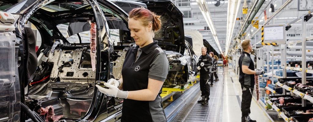 Woman inspecting car chassis with handheld device on a Mercedes-Benz assembly line