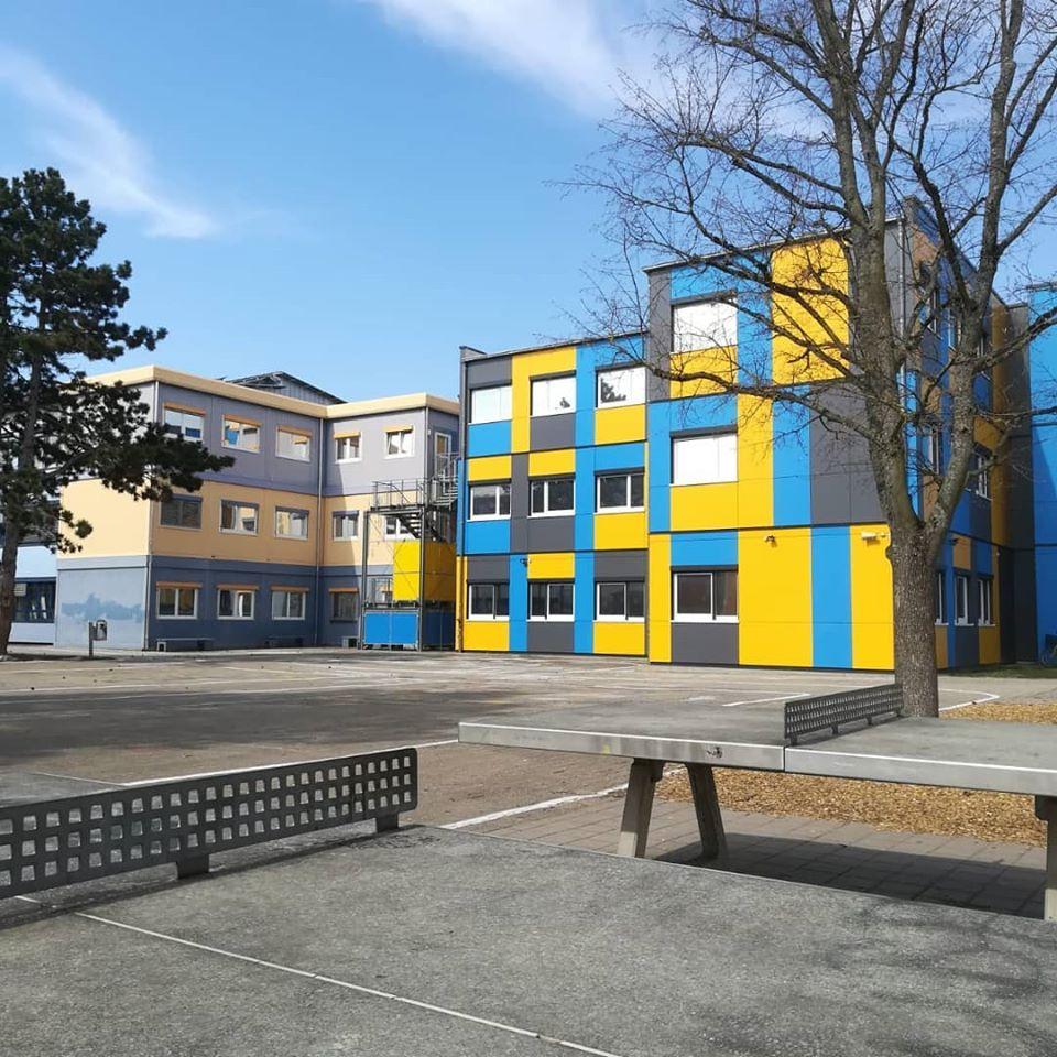 Modular container building with yellow, blue, and gray panels, featuring outdoor ping-pong tables in front