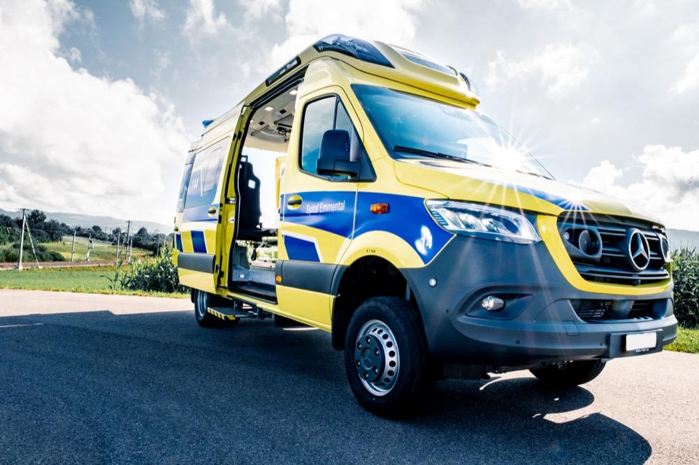 Yellow and blue Mercedes Sprinter ambulance van with open side door revealing interior medical setup