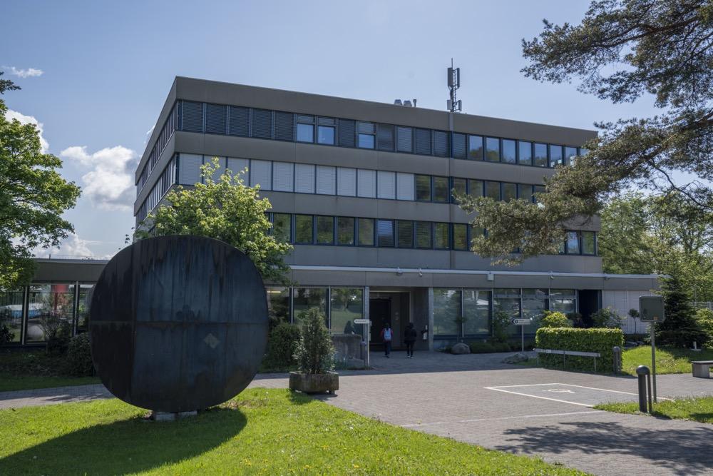 Modern four-story office building with round metal sculpture in front and trees around