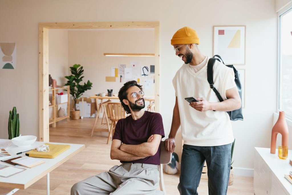 Two casually dressed men laughing together in a living room holding a smartphone.