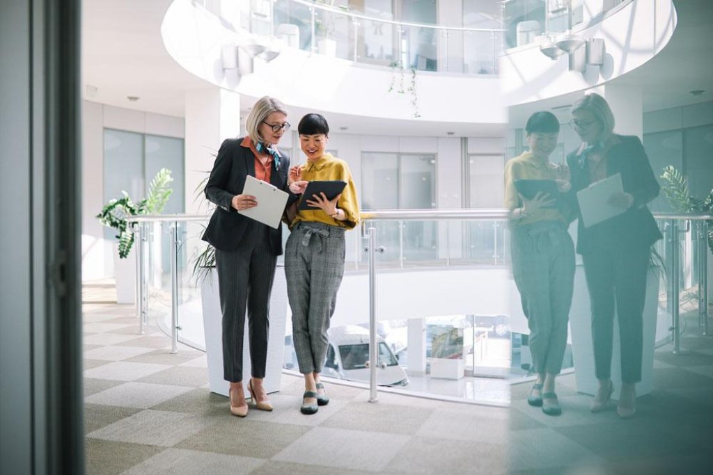Zwei Geschäftsfrauen in einem Bürogebäude, die ein Thema auf einem Tablet-Computer besprechen.