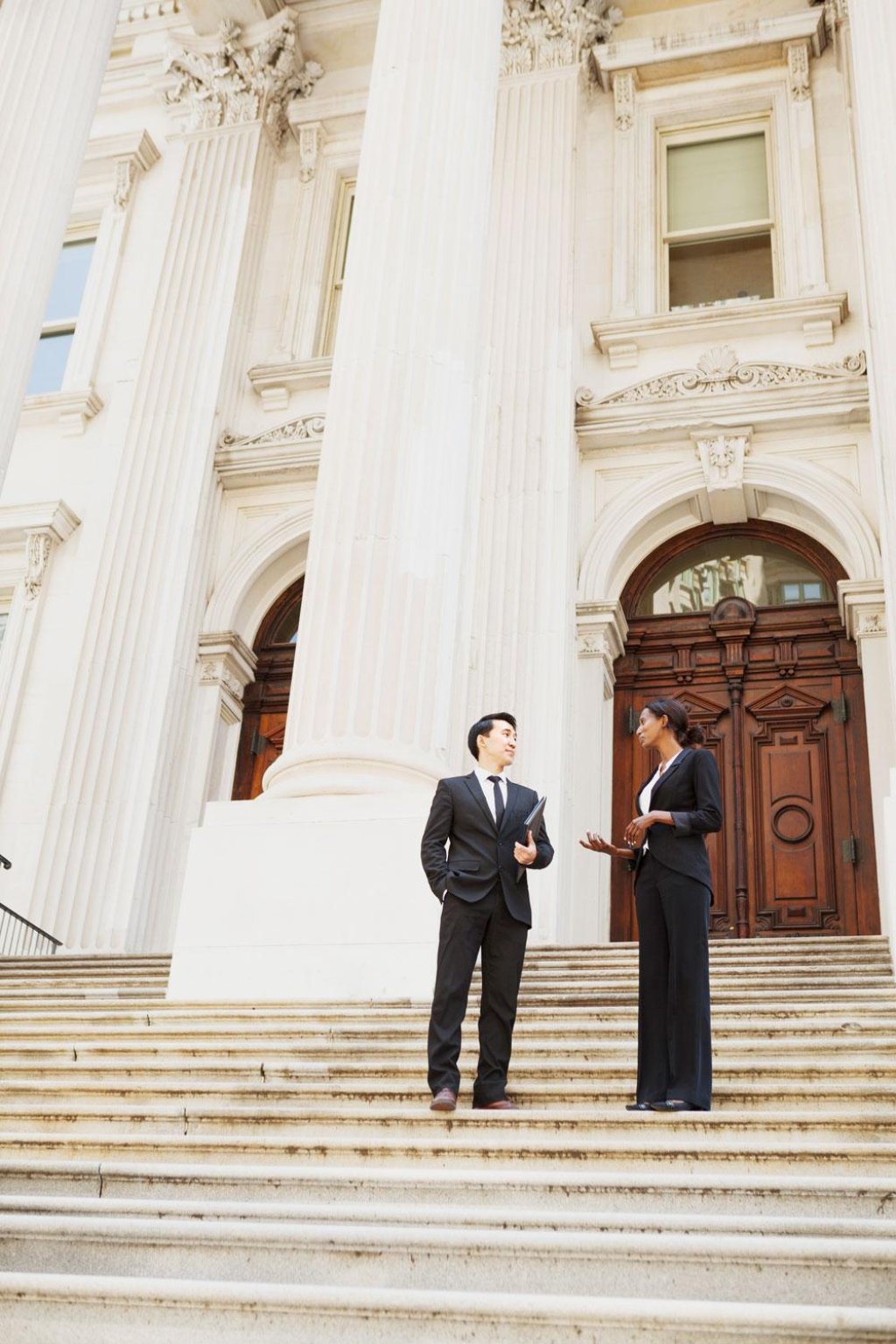 Man and woman in suits chatting on the stairs of a public building.