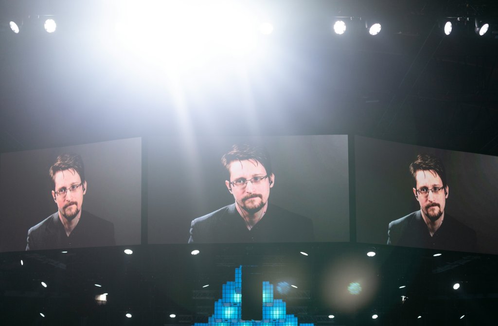 Edward Snowden en tres pantallas grandes durante una aparición por video en un evento.
