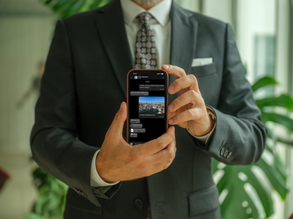A man in a business suit shows a smartphone displaying a messaging conversation.