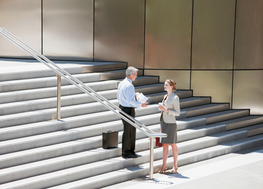 Man and woman in formal clothing chatting on the stairs of a public building.