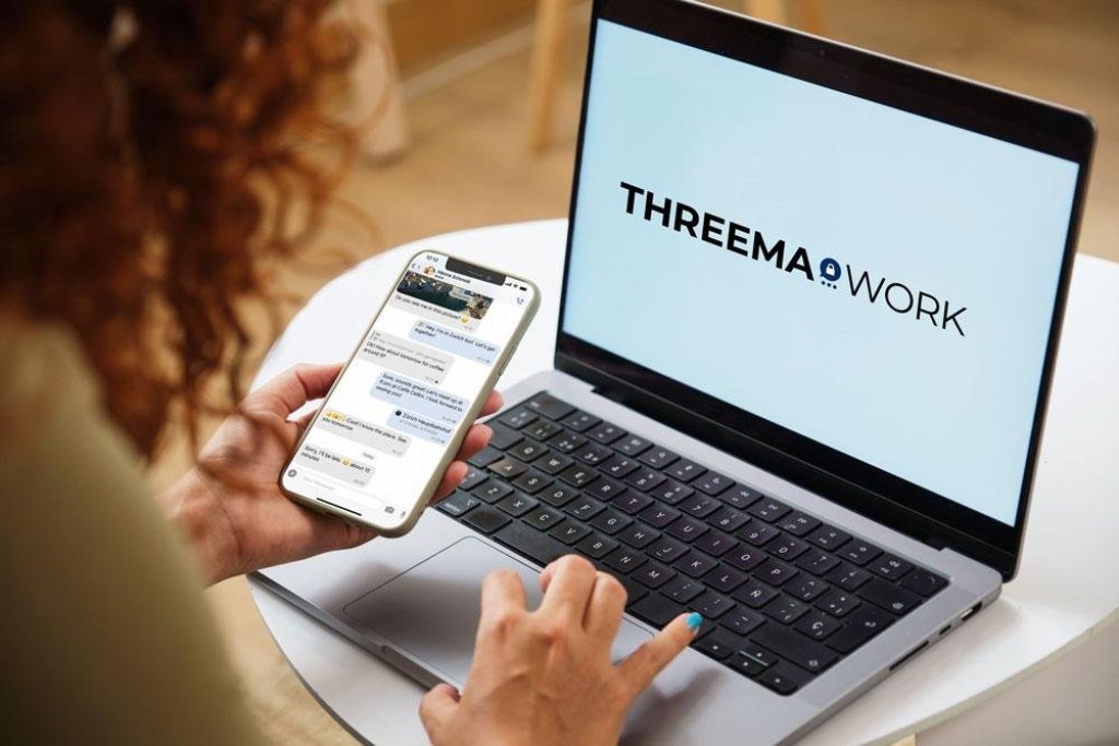 Woman operating a laptop and smartphone displaying a Threema logo and chat.