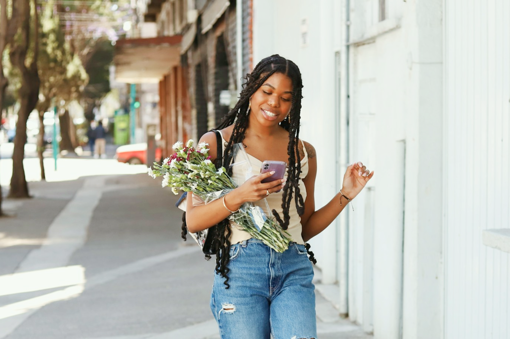 Smiling woman checking her smartphone while carrying a bouquet of flowers.