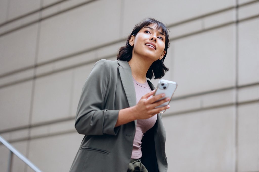 Businesswoman checking her smartphone while walking up outdoor stone steps in a blazer.