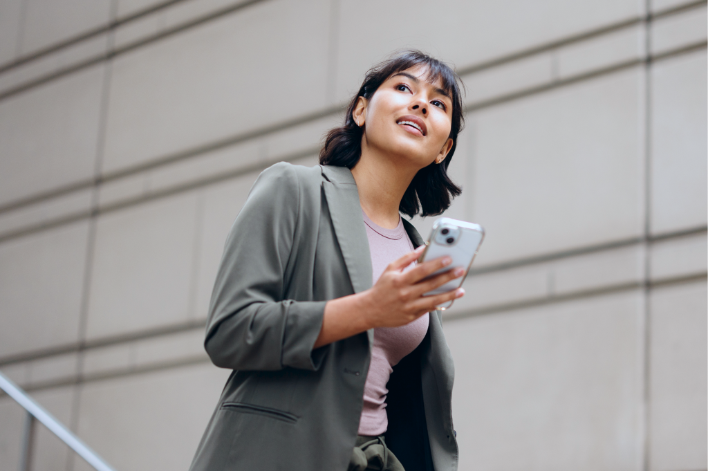 Mujer de negocios con blazer revisa su smartphone mientras sube una escalera exterior.