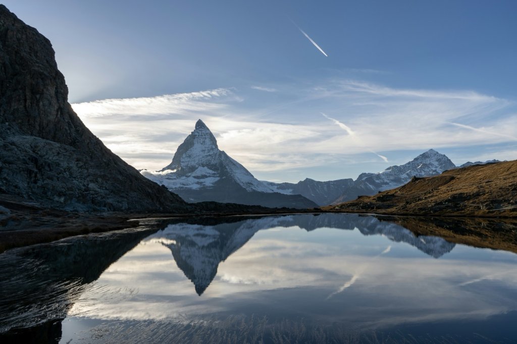 Snow-capped Matterhorn peak reflected in a calm alpine lake under blue sky.