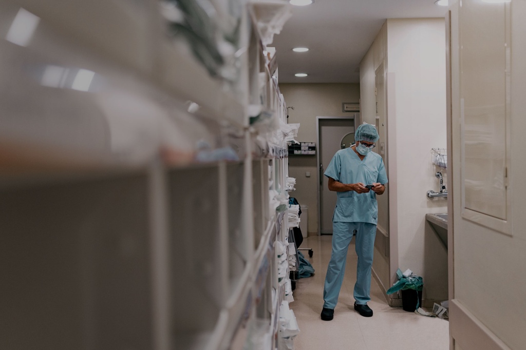 Surgeon in medical clothing in a hospital using a smartphone for communication.