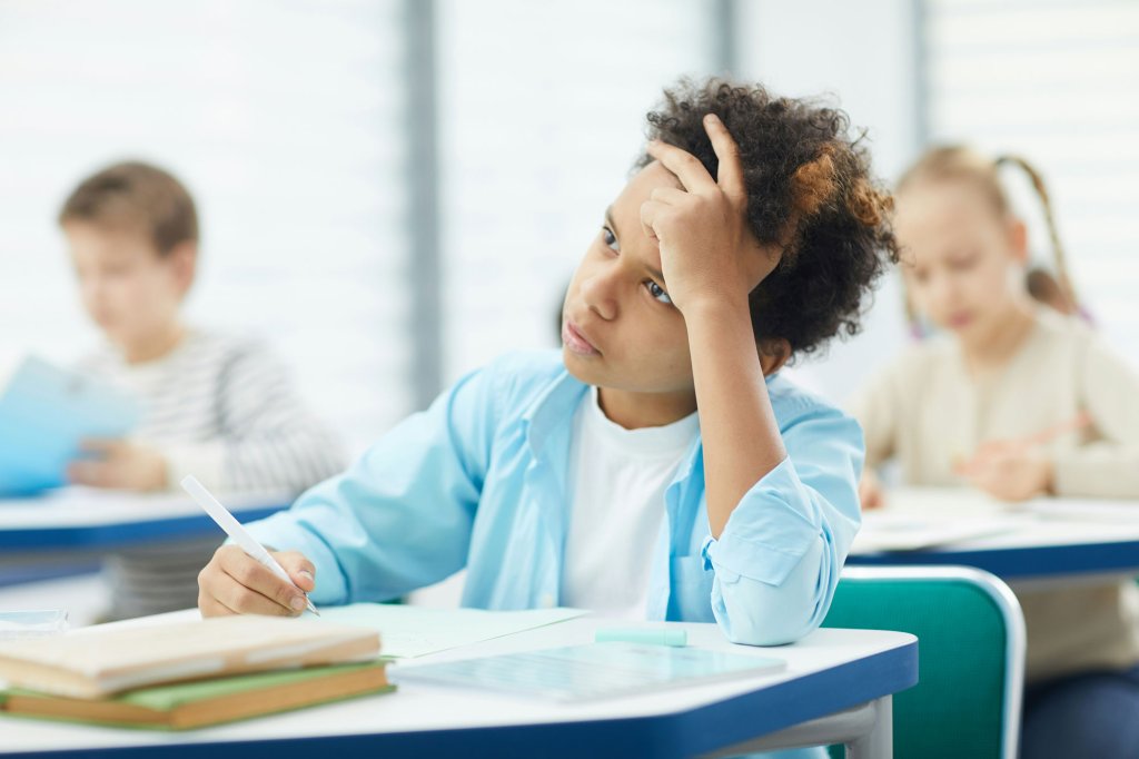 Schüler denkt nach, während er im Klassenzimmer schreibt.