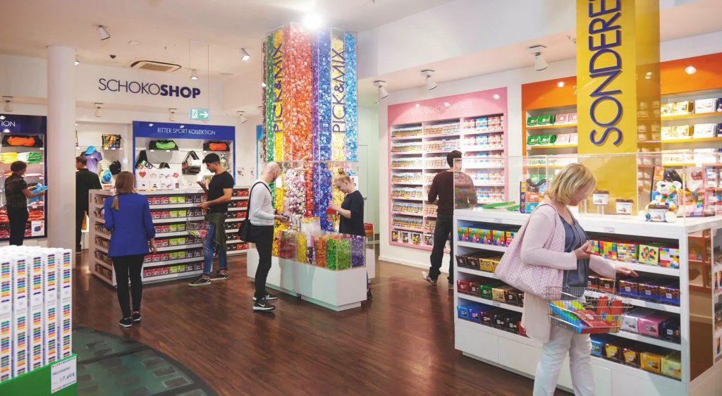 Bunter Schokoladenshop mit Kunden beim Auswaehlen von Produkten und individuellen Mischungen.