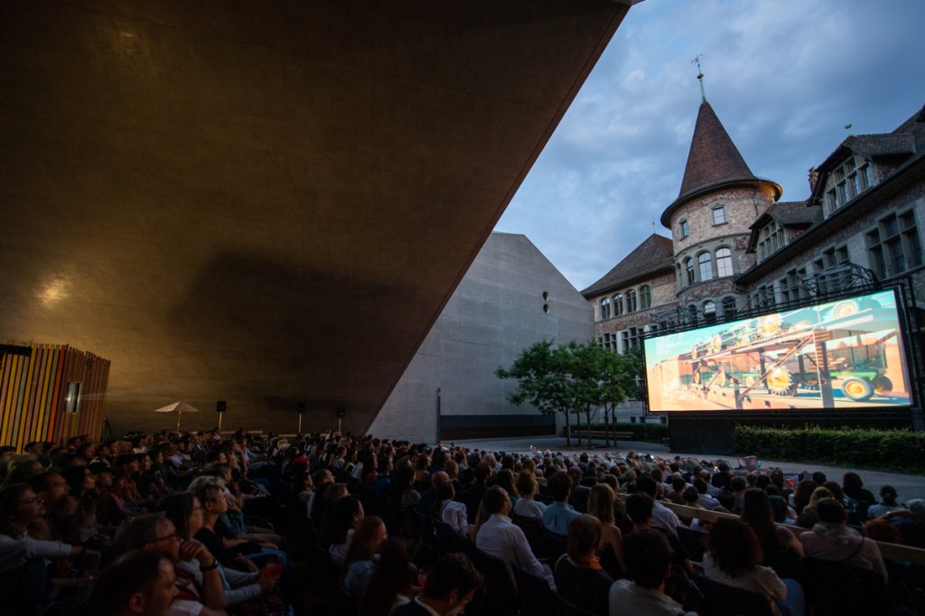 Menschen sitzen abends unter freiem Himmel in Z&uuml;rich und schauen gemeinsam einen Film auf einer gro&szlig;en Outdoor-Leinwand.