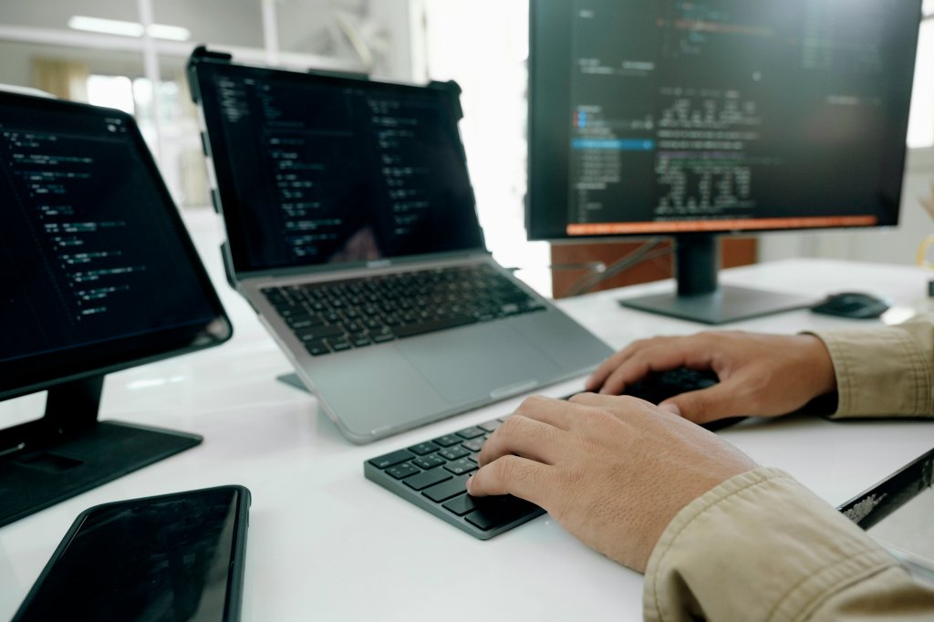 B&uuml;roangestellter an einem Schreibtisch mit Laptop, Bildschirm und Tablet arbeitet.