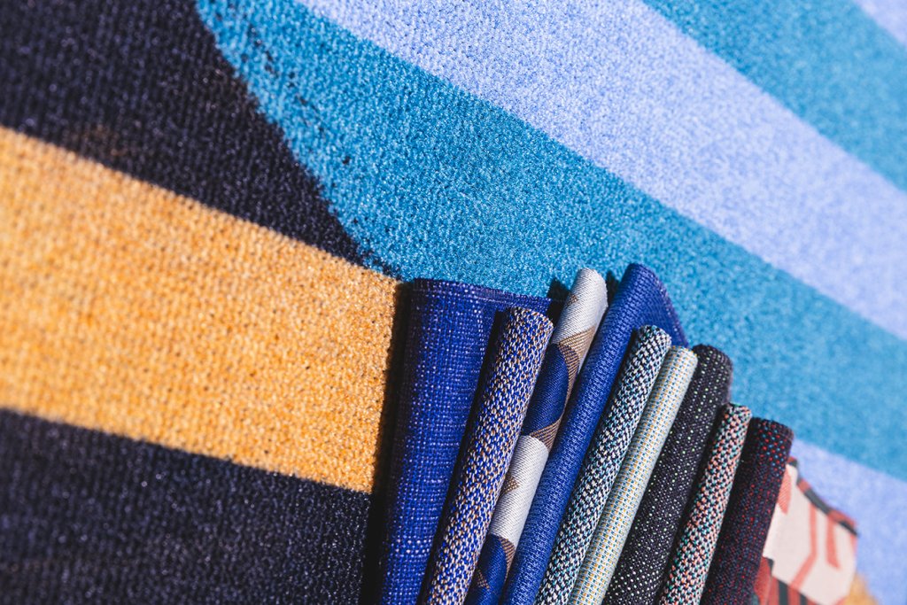 Fabric samples from Lantal Textiles AG in various colors and weave patterns displayed against a colorful textile background.