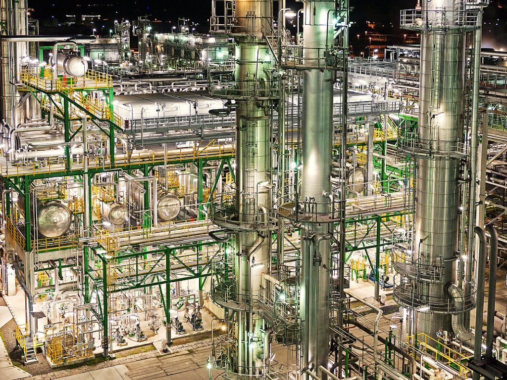 Night view of PCK refinery with illuminated industrial structures and pipelines.