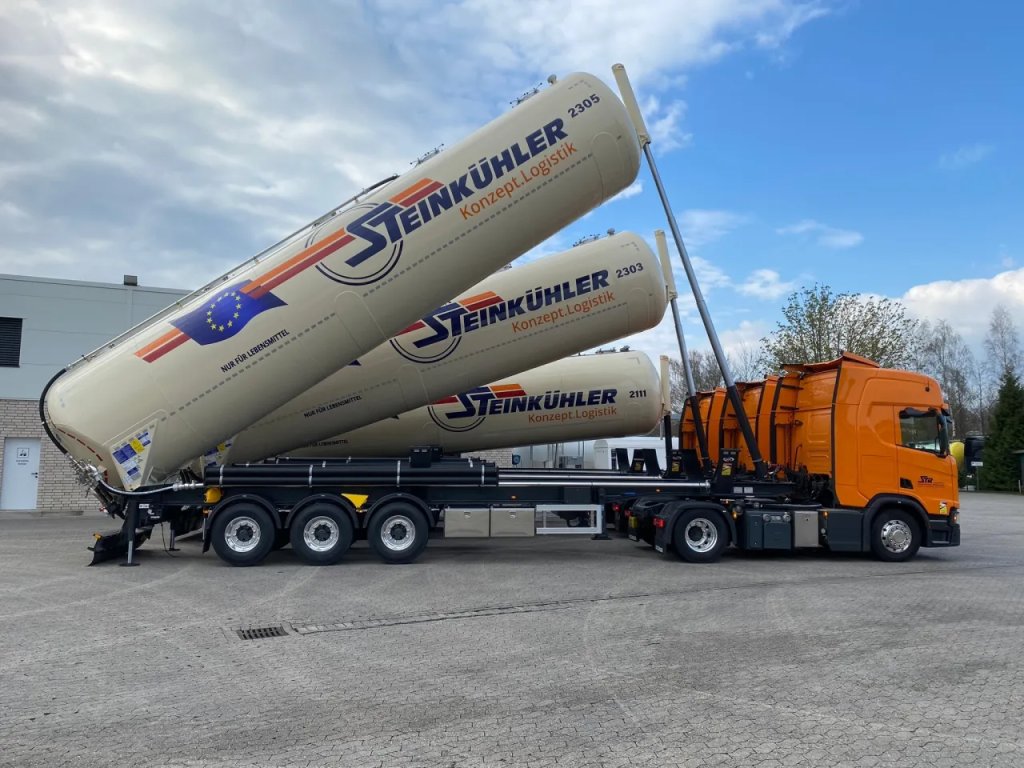 Semi-remorque citerne silo Steink&uuml;hler pour produits alimentaires, relev&eacute;e pour le d&eacute;chargement, avec tracteur Scania orange.