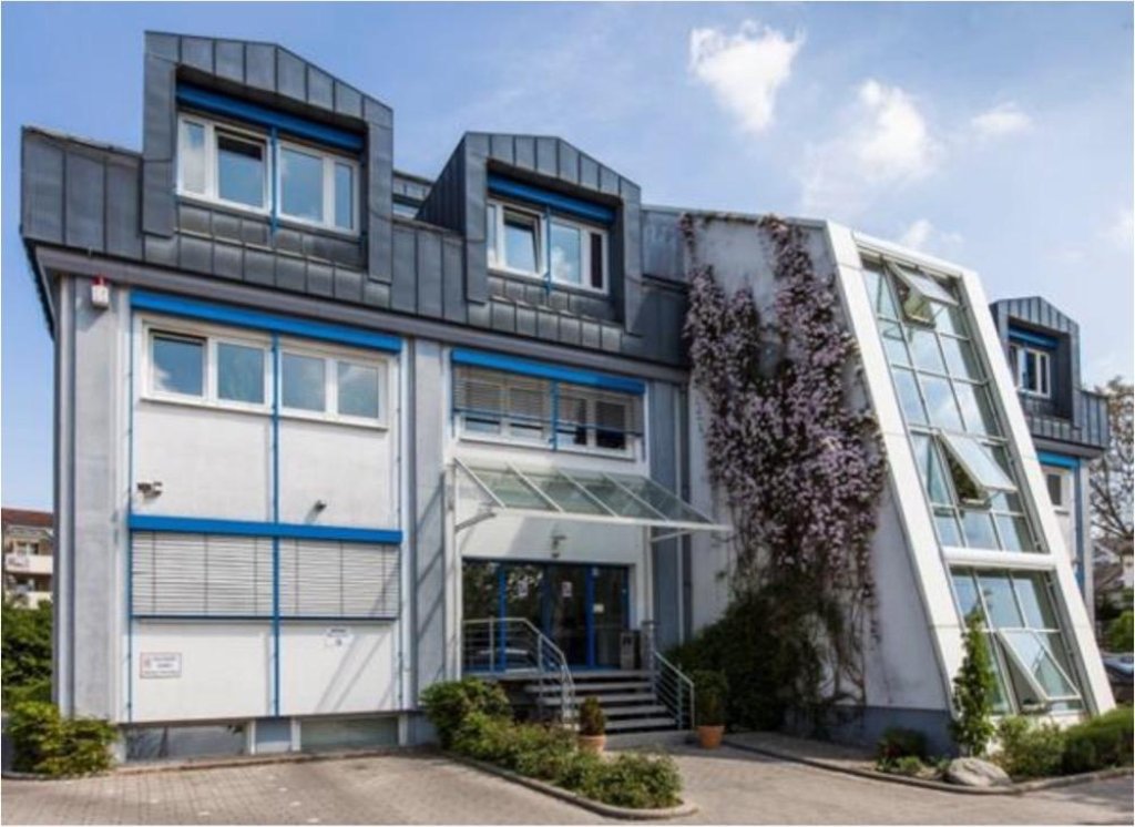 Edificio de oficinas gris y azul con fachada de vidrio inclinada y enredadera con flores moradas.