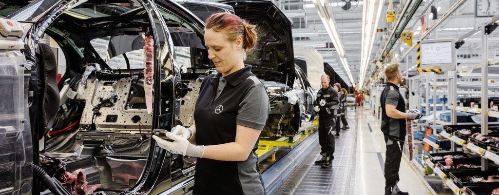 Woman inspecting car chassis with handheld device on a Mercedes-Benz assembly line.