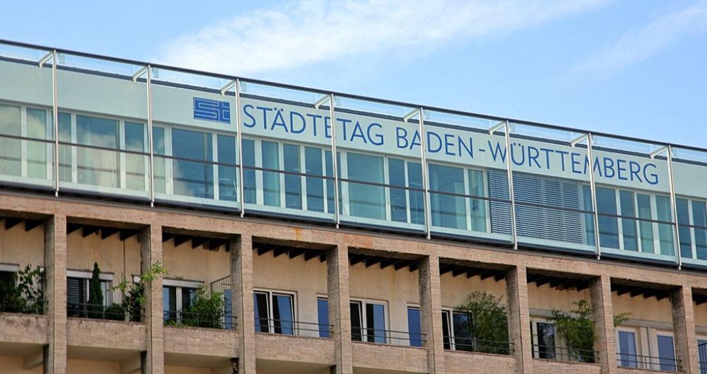 Fachada de edificio de oficinas moderno con el r&oacute;tulo 'St&auml;dtetag Baden-W&uuml;rttemberg' en la parte superior bajo un cielo azul.