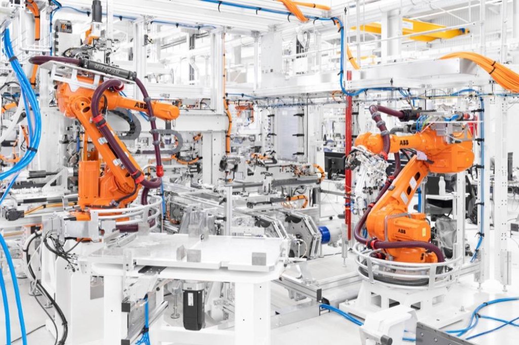 Orange ABB robotic arms on white automated assembly line with cables.