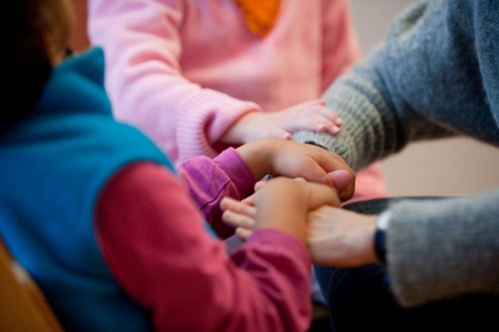 Children and adult holding hands in a supportive gesture.